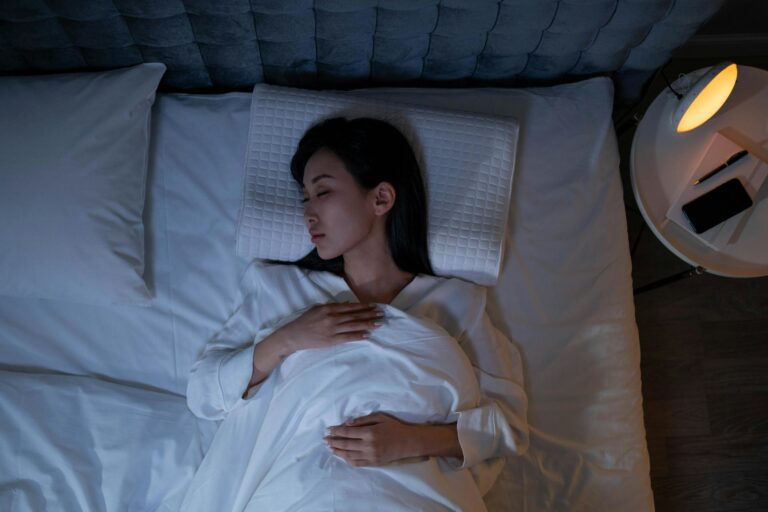 Woman sleeping peacefully in bed with smartphone on nightstand at night