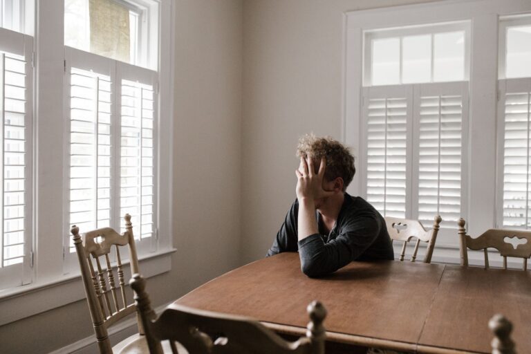 A man sitting alone at a farmhouse kitchen table with his head in his hand